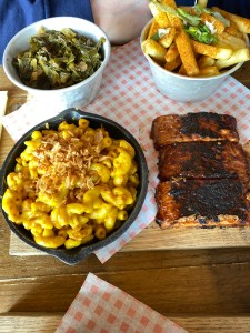 Board of food, collard greens, vegan mac and cheese, fries and tempeh BBQ ribs