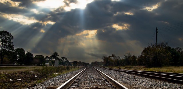 train tracks leading into the distance, sunlight through the clouds
